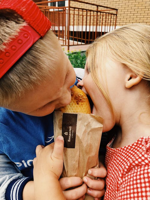 Photo of Two Kids Biting a Piece of Bread