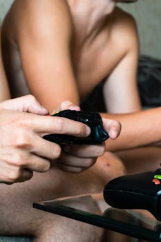 Focused close-up shot of hands holding a gaming controller, with unrecognizable gamers playing indoors.
