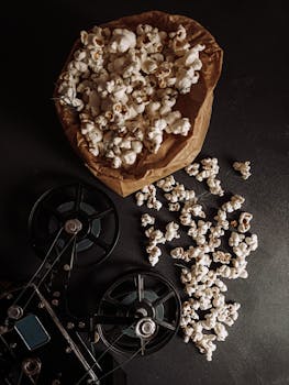 Top view of popcorn in a paper bag with vintage film reels on a dark surface.