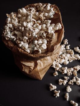 Aesthetic close-up of fresh popcorn overflowing a brown paper bag on a dark surface.