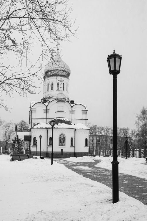 Free A serene monochrome photo of a snow-covered Orthodox church with street lamps in a winter landscape. Stock Photo