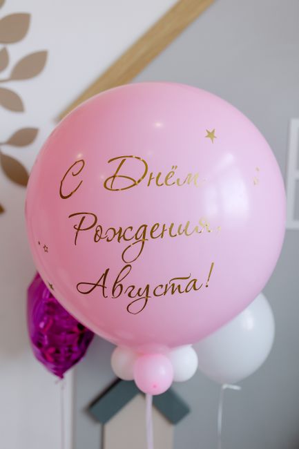Pink and purple balloons with Russian birthday greeting. Indoors celebration setup.