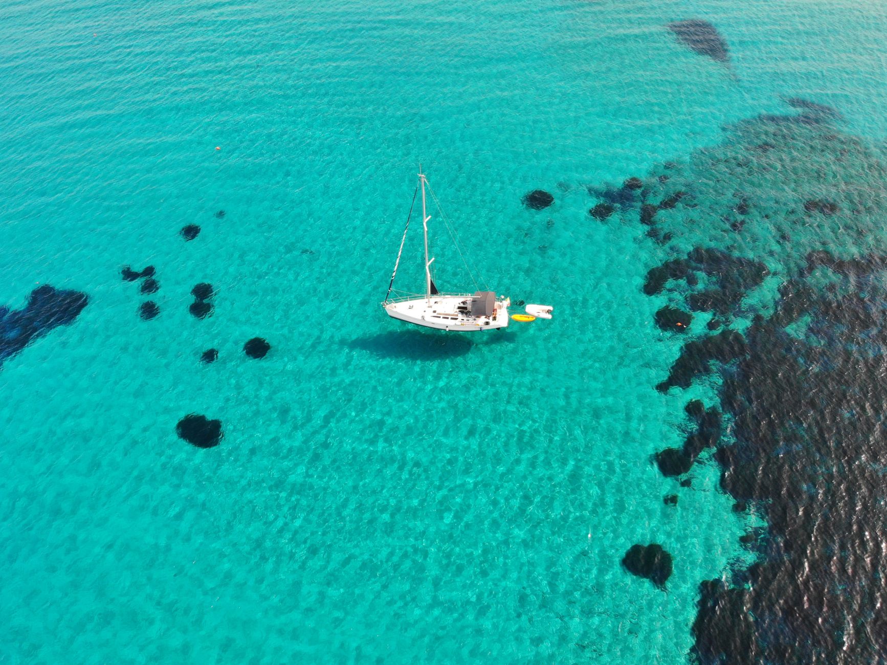 Captivating aerial shot of a sailboat in the turquoise waters near Geremeas, Sardegna, Italy.