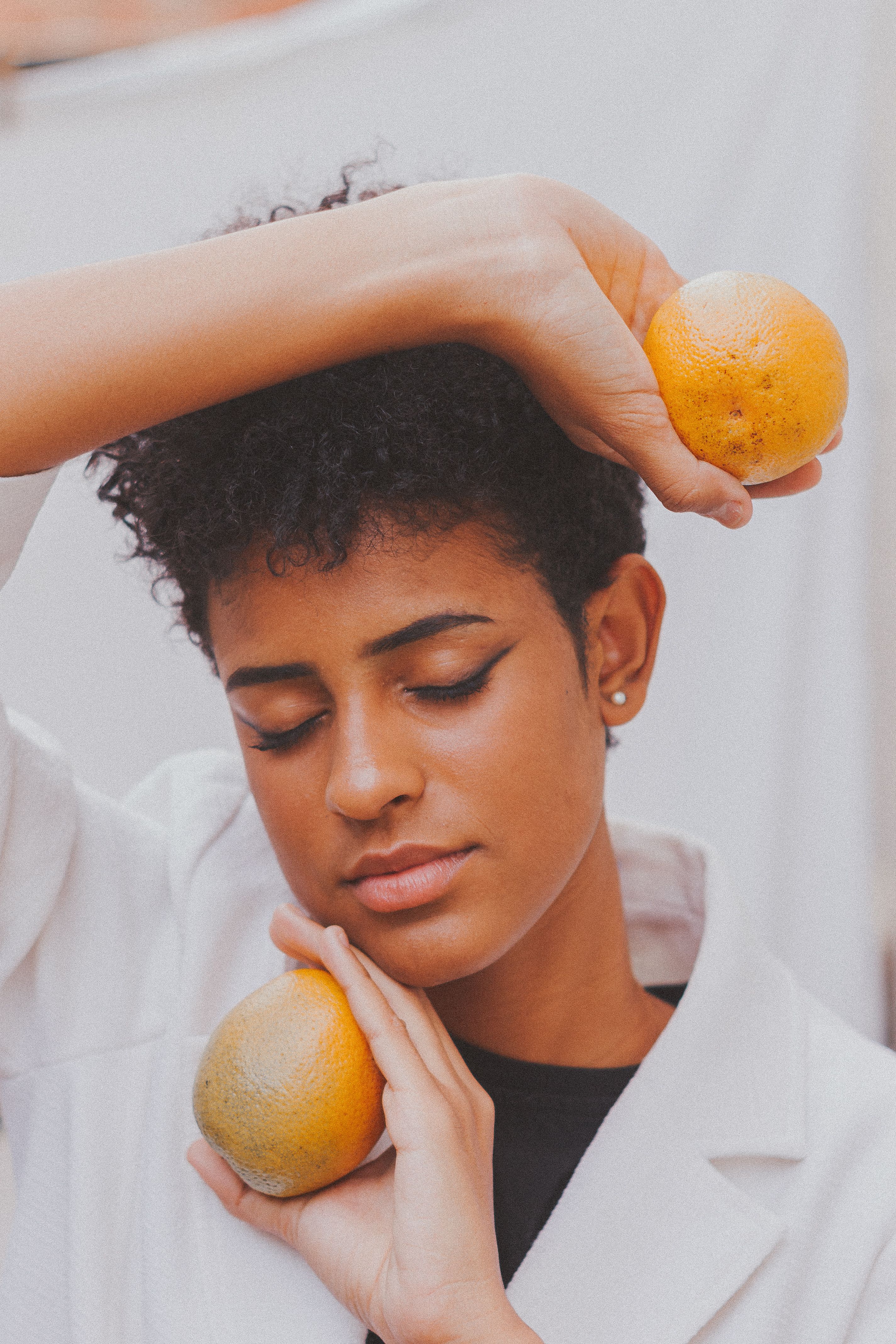 A serene portrait of a woman with closed eyes holding oranges against a soft backdrop.
