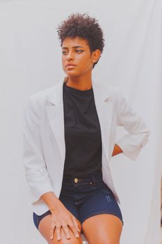 Portrait of a confident black woman in a white blazer and curly hair sitting outdoors.