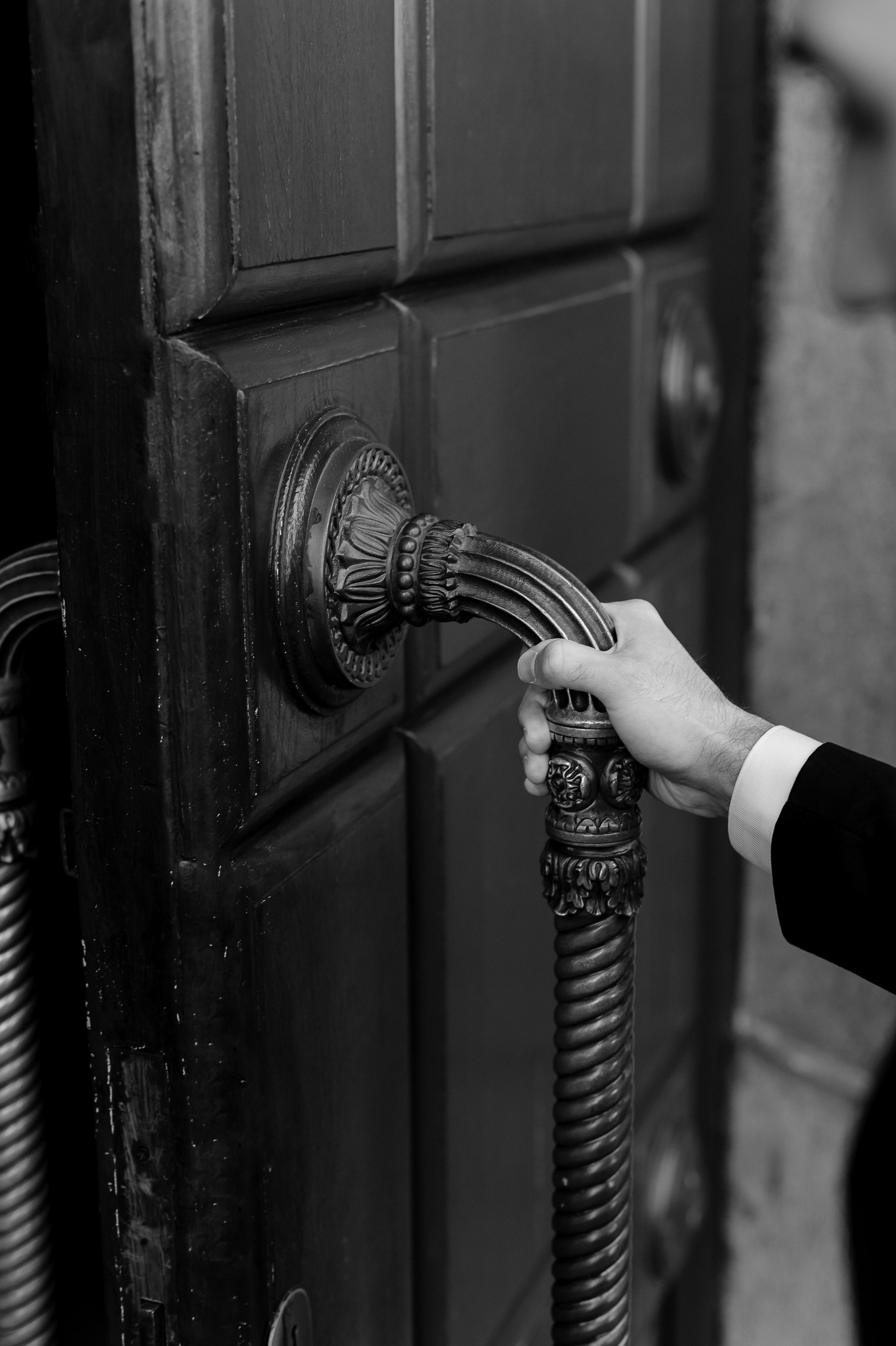 Black and white close-up of a hand holding an ornate door handle, showcasing elegance and style.