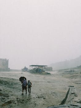 Two people walking with an umbrella in a foggy and rainy outdoor setting, capturing a moody atmosphere.