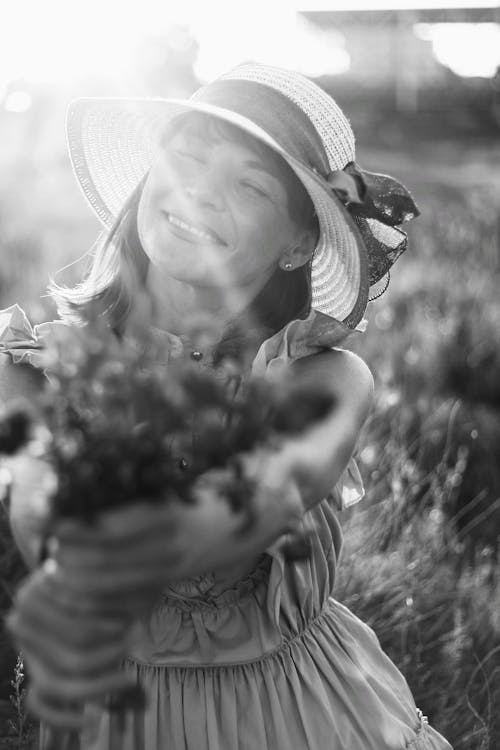 Grayscale Photo of Smiling Woman Holding a Plant 