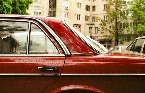 Free Close-up of a vintage red sedan with rain drops, parked in a city environment. Stock Photo