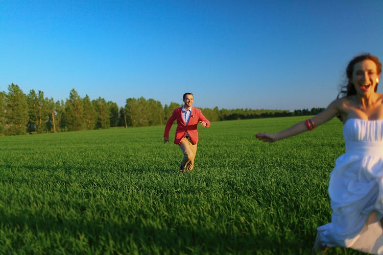 A Man Chasing His Woman On The Grass Field