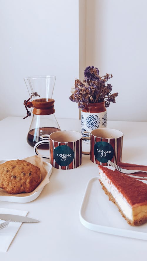 Free Sweet oat cookies with piece of delicious cheesecake placed near cups of coffee brewed in chemex near vase of dried flowers Stock Photo