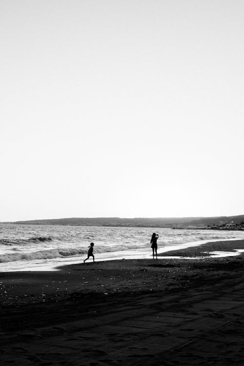 Grayscale Photo of Two People Standing at the Beach Shore