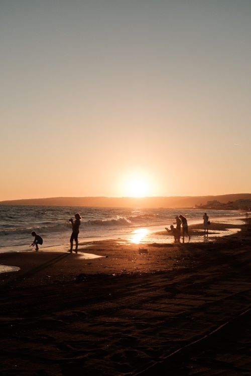 Free People enjoying a serene sunset at a sandy beach, coastal vibes in warm hues. Stock Photo