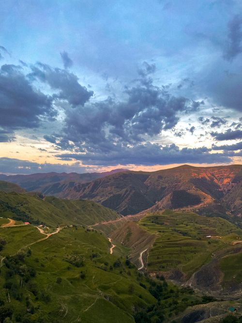 Free A breathtaking view of rugged mountains under a dramatic cloudy sky, captured at sunset. Stock Photo