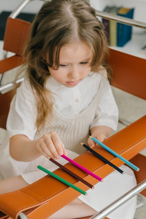 Free Young girl concentrating on arranging colored pencils creatively indoors. Stock Photo