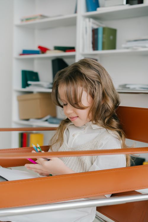 Free A young girl sits in a chair at home, involved in artistic activities, showcasing creativity and learning. Stock Photo