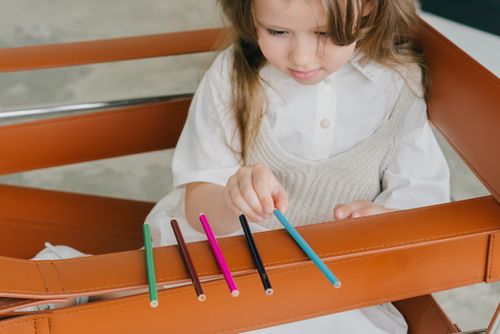 Free A young girl attentively arranging colored pencils on a leather chair. Stock Photo