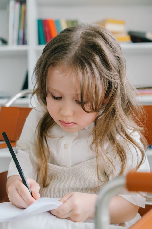Free Adorable young Caucasian girl focused on writing at a desk indoors. Captivating and educational. Stock Photo