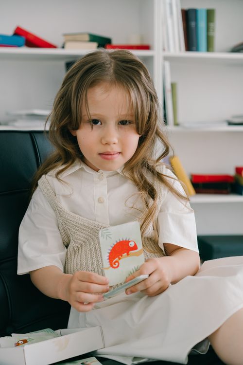Free A young girl sits indoors holding a colorful art card, smiling gently. Stock Photo