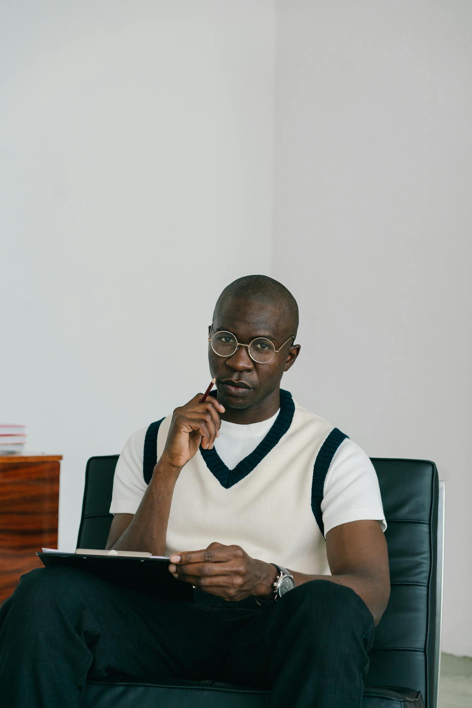 Bald man wearing eyeglasses, sitting with a notebook, looking serious indoors.