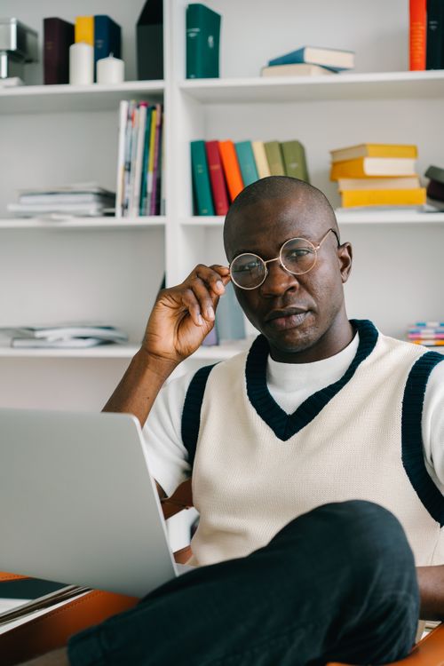 Free Confident man with glasses using laptop in a modern office with bookshelves. Stock Photo