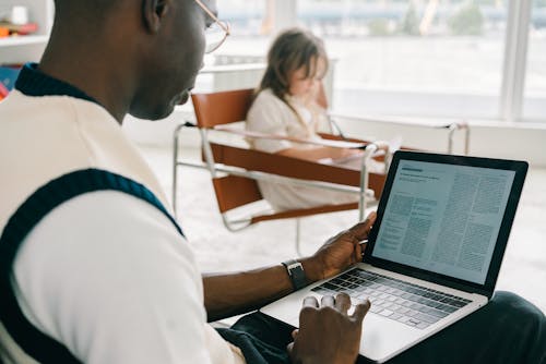 A Man in White Polo Shirt Sitting on a Chair while Using a Laptop