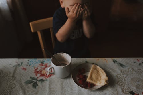 Photograph of a Kid Covering His Eyes During Breakfast