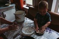A young child and adult hands kneading dough in a cozy kitchen setting. Warm, intimate family moment.