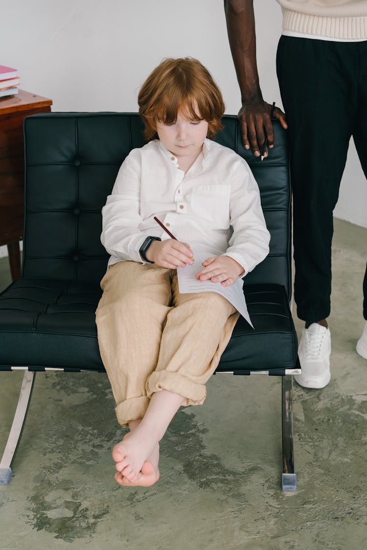 Photo Of A Boy Writing On A Piece Of Paper