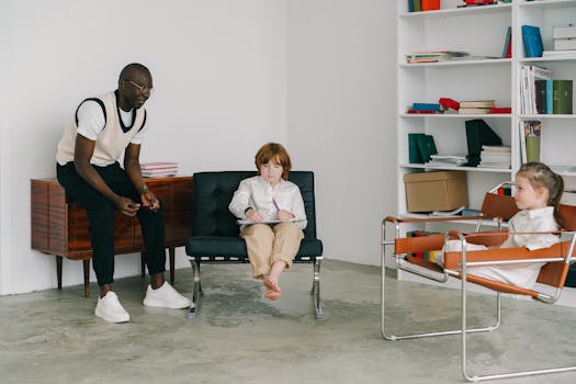 A teacher guides children in a classroom with books and modern chairs, fostering education and development.