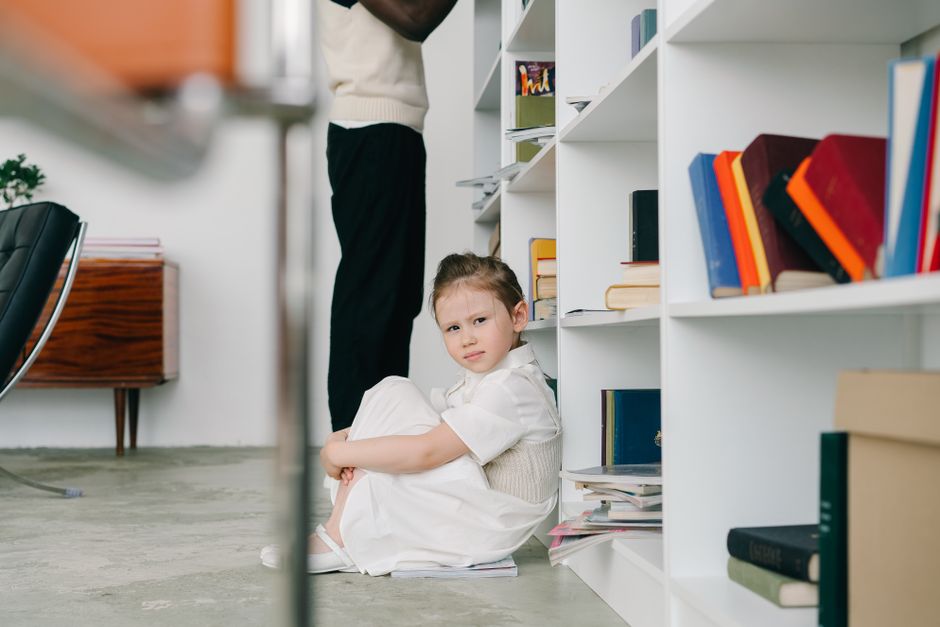 Photo by Mikhail Nilov on Pexels A young girl in a white dress sitting by a bookshelf in a modern library setting. - Photo by Mikhail Nilov on Pexels