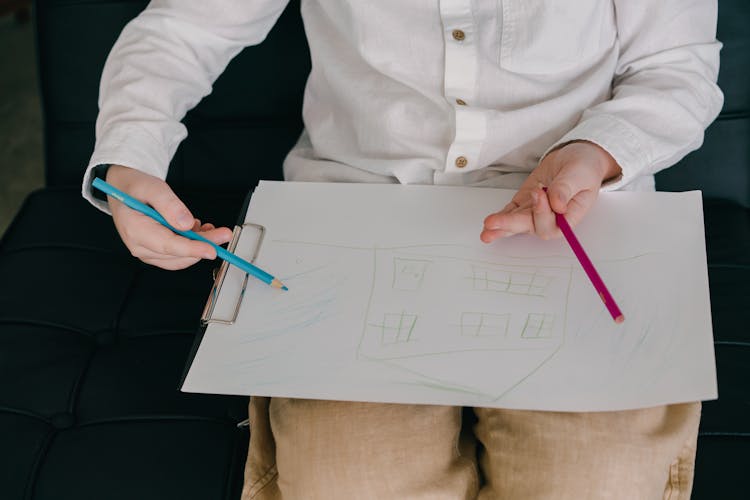 Close-Up Shot Of A Child Drawing A House On A Paper