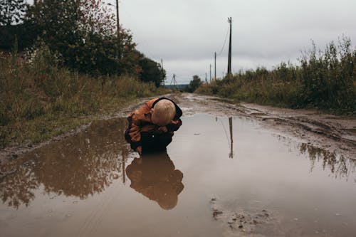 Photograph of a Kid Crouching in a Puddle