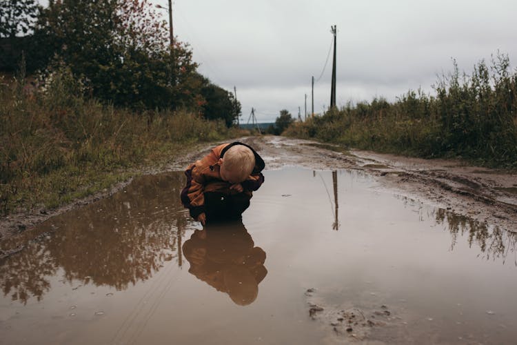 Photograph Of A Kid Crouching In A Puddle