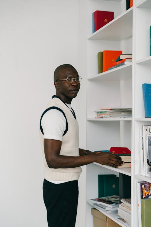 Man in White and Black Crew Neck T-shirt Standing Near White Book Shelves