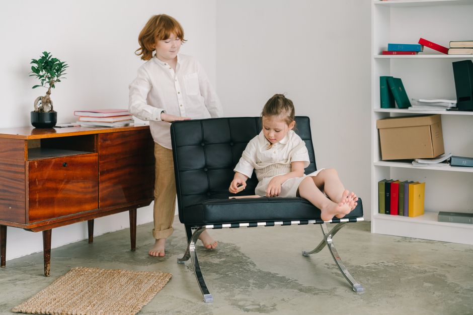Dos niños en una habitación contemporánea, interactuando con un libro y muebles.