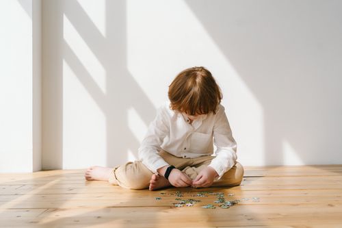 Free Child sitting on wooden floor concentrating on puzzle pieces, bathed in warm natural light. Stock Photo