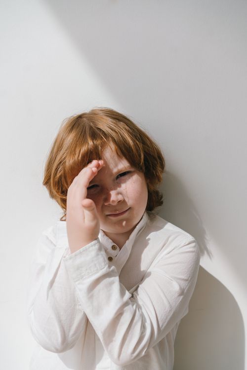 Free A young redhead child wearing a white shirt, squinting in bright sunlight against a plain background. Stock Photo