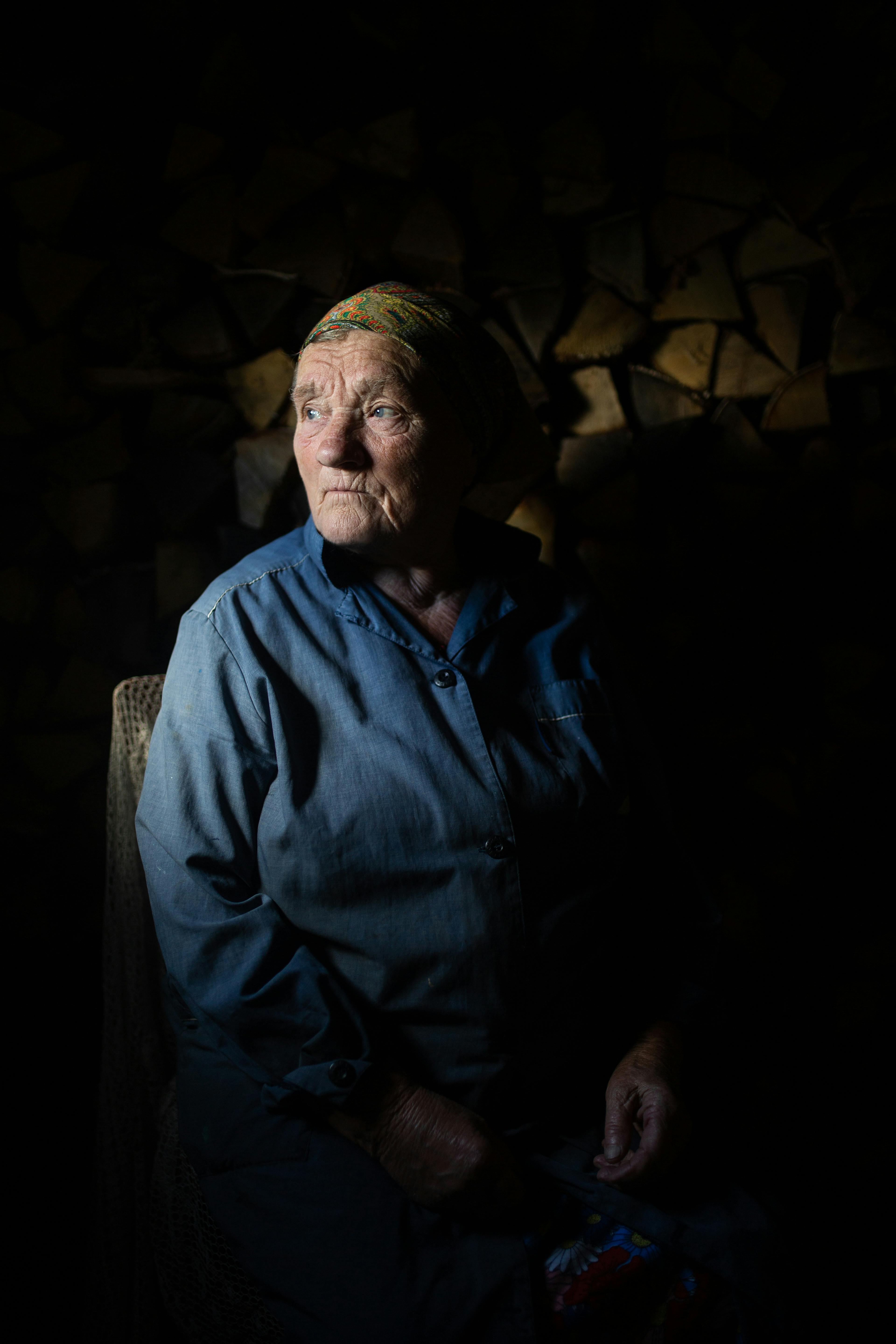 A contemplative side portrait of a senior woman sitting in low light.