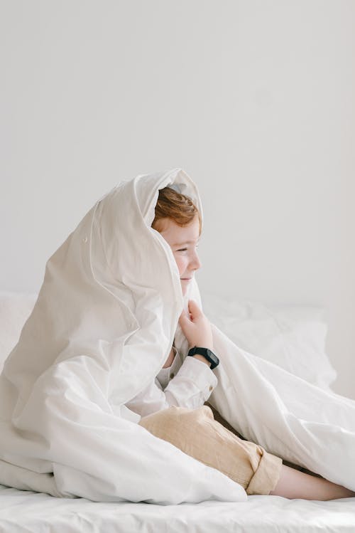 Photo of a Boy Under a White Blanket