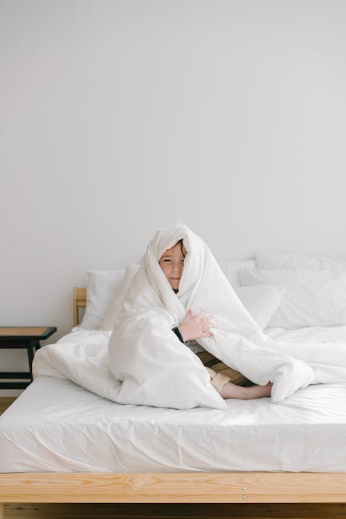 Child Covered with With Blanket while Sitting on Bed