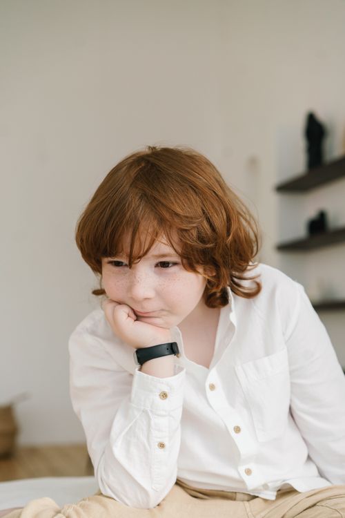 Free A thoughtful red-haired boy wearing a white shirt poses indoors, showcasing a cute and curious expression. Stock Photo
