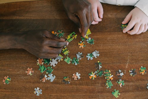 Close-Up Shot of Two People Playing Jigsaw Puzzle on a Wooden Surface