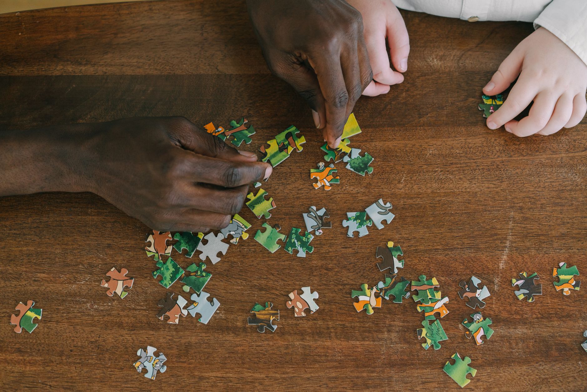Two hands collaborating to solve a jigsaw puzzle on a wooden surface, emphasizing teamwork.