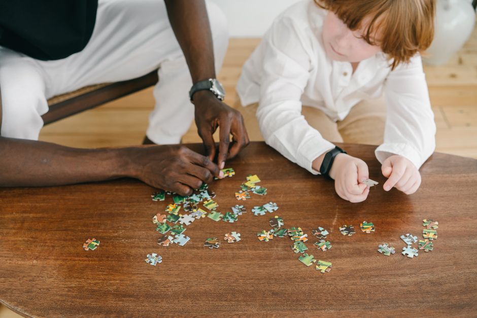 Adult and child bonding while solving a puzzle on a wooden table.