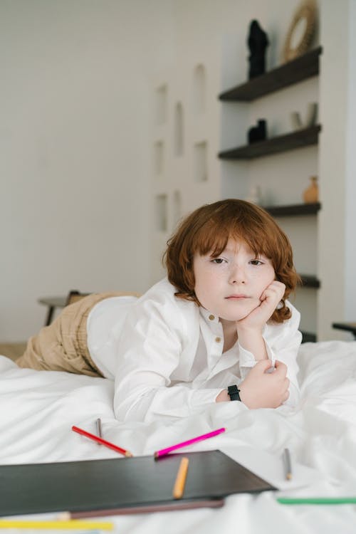 Boy in White Long Sleeve Shirt Lying  on Bed