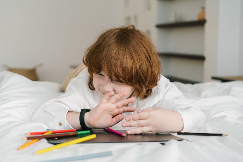 Photo by Mikhail Nilov on Pexels A young redheaded boy lying on a bed, playing with colored pencils indoors, expressing creativity. - Photo by Mikhail Nilov on Pexels