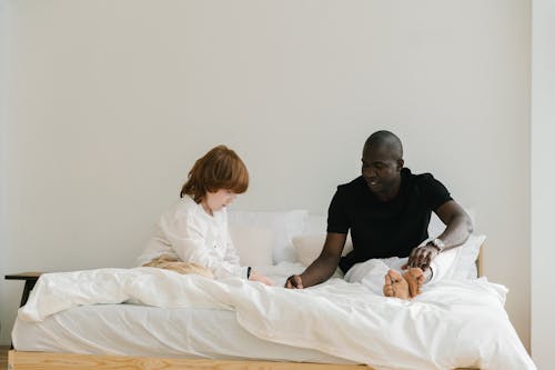 Free A Man Talking to His Son while Sitting on the Bed Stock Photo