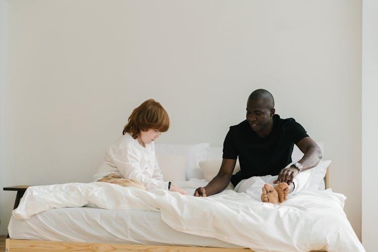 A Man Talking To His Son While Sitting On The Bed