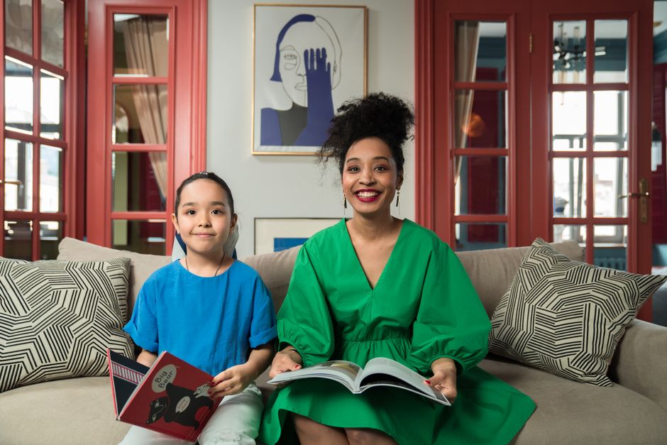 A smiling mother and daughter reading books together on a comfortable sofa in a bright, inviting room.